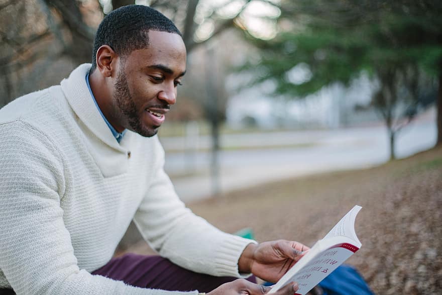 Man smiling and reading a book outside